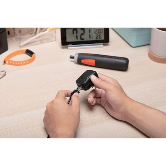 Photo of BLACKDECKER BD40K27 cordless screwdriver on desk, hands connecting charging cable to charger.