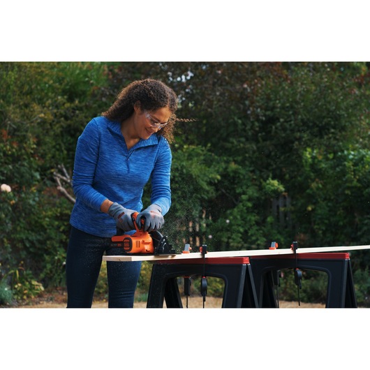 Person using BLACKDECKER BDCCS18N cordless circular saw to cut wood outdoors on sawhorses.