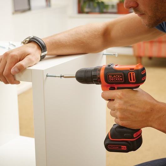 Photo of BLACK+DECKER BDCDD12A80T cordless drill in use, driving a screw into white furniture.