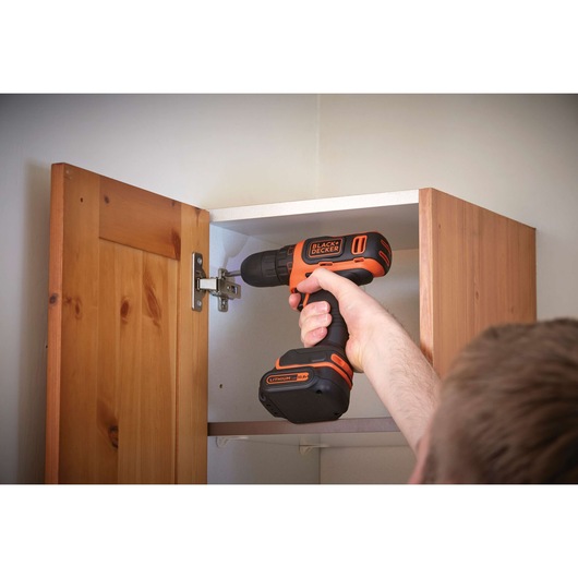 Photo of BLACKDECKER BDCDD12 cordless drill being used to install a hinge in a wooden cabinet.