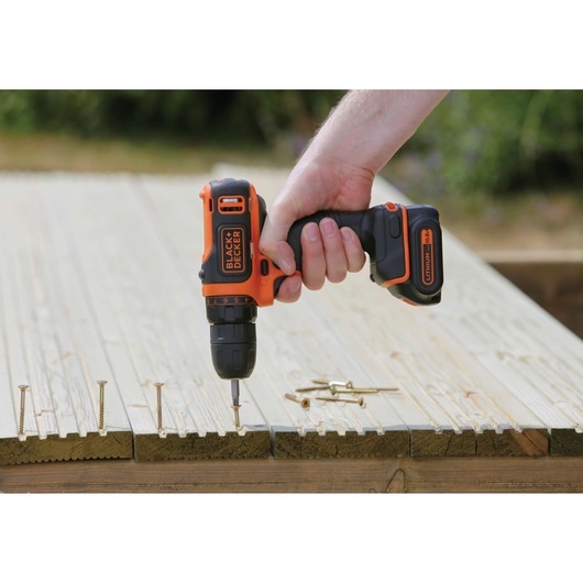Photo of BLACK+DECKER BDCDD12 cordless drill in use, driving screw into light wood with several screws nearby.