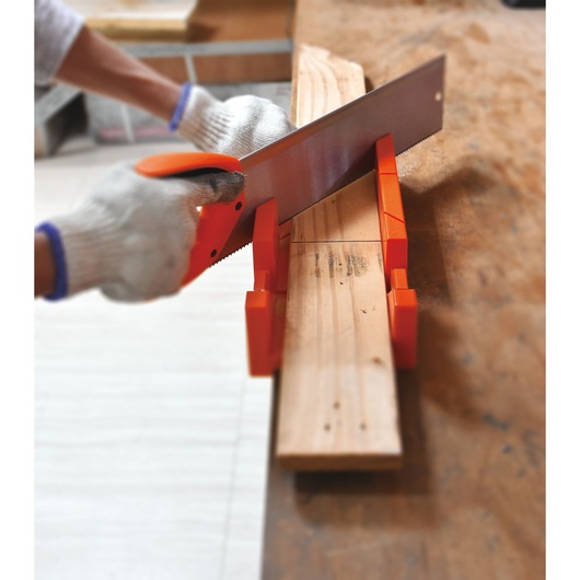 BLACKDECKER BDHT20346 hand saw cutting wood with orange miter box on workbench, close-up action view.