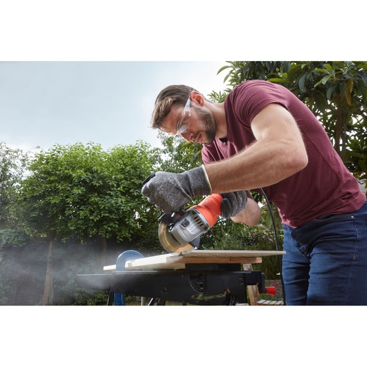 BLACKDECKER BEG010 cordless circular saw cutting wood outdoors, side angle, user wearing gloves.