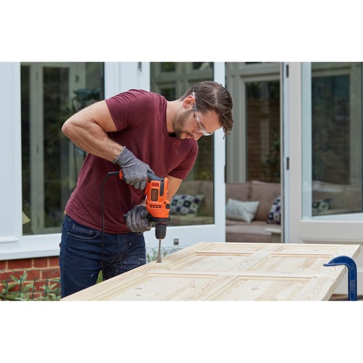 Photo of BLACKDECKER BEH200 corded drill in use on a wooden door, person wearing gloves and safety glasses.