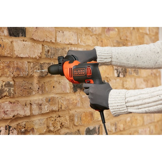 BLACK+DECKER BEH710 corded hammer drill in use drilling into brick wall, black and orange design.