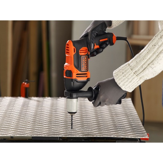 Photo of BLACKDECKER BEH850 hammer drill in use drilling metal sheet, close-up of hands wearing gloves.