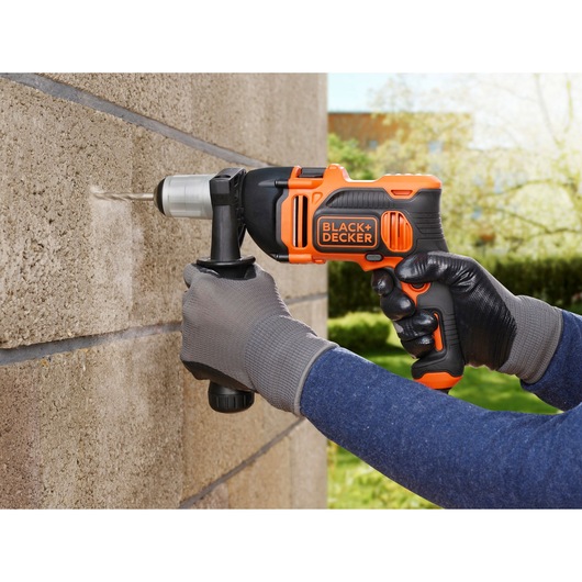 BLACK+DECKER BEH850 hammer drill, orange and black, in use on concrete wall outdoors.