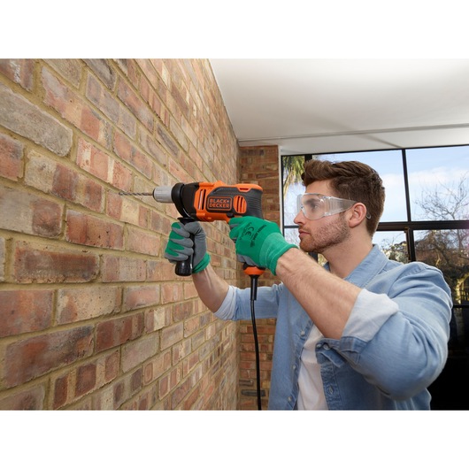 Photo of BLACKDECKER BEH850 corded drill being used on a brick wall, person wearing green gloves.