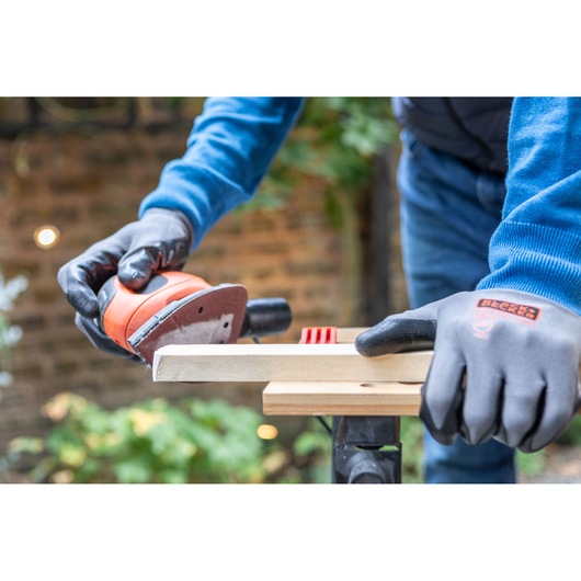 BLACKDECKER BEW230 sander in use on wood, person wearing BLACKDECKER gloves outdoors.