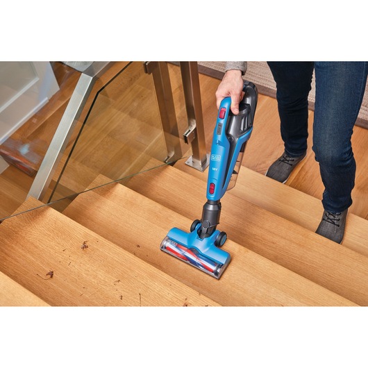 BLACKDECKER BHFE520J cordless stick vacuum cleaning wooden stairs, blue body and red accents.