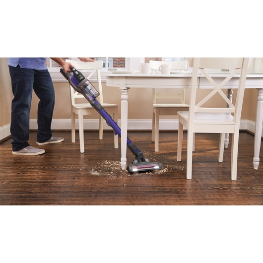 Photo of BLACKDECKER BHFEV182CP cordless stick vacuum cleaning debris from wooden floor near dining table.