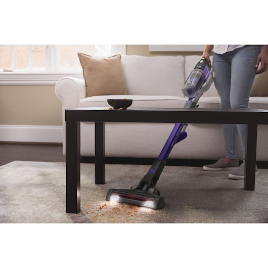 BLACKDECKER BHFEV362DP cordless stick vacuum cleaning crumbs from carpet under coffee table in living room.