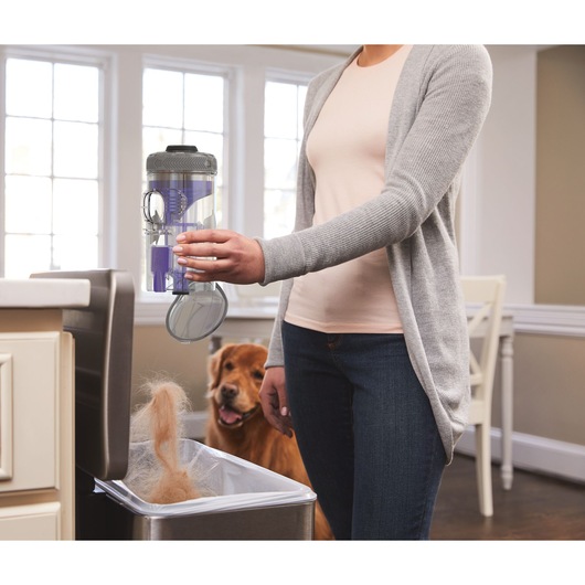 BLACKDECKER BHFEV362DP vacuum cleaner canister being emptied into kitchen trash bin, pet hair visible, indoor setting.
