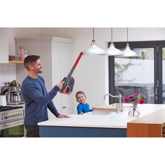 BLACKDECKER BHHV315J cordless vacuum cleaner with long nozzle attachment used to clean pendant lights in modern kitchen.