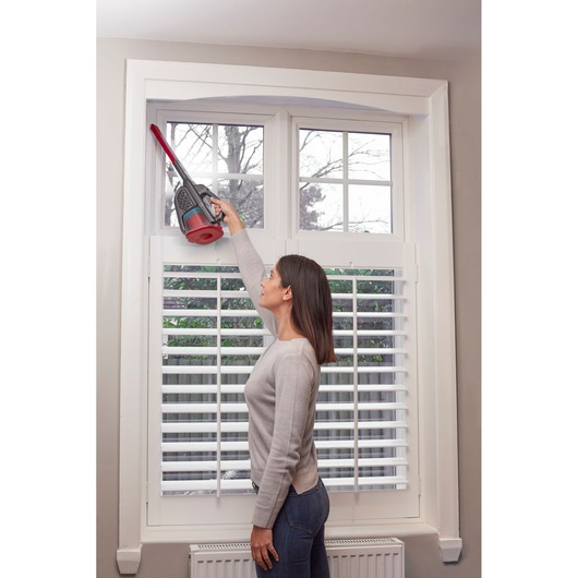 BLACKDECKER BHHV315J handheld vacuum cleaning window frame with long nozzle in home setting.