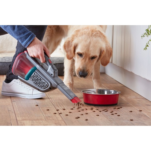BLACKDECKER BHHV315J handheld vacuum cleaning pet food near red bowl on wooden floor, side angle