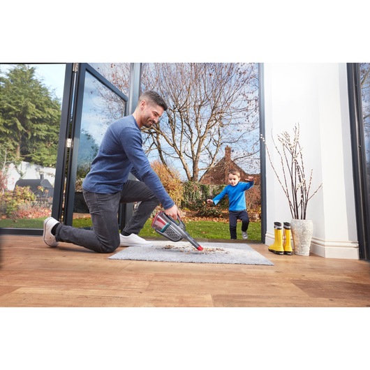 BLACKDECKER BHHV315J handheld vacuum cleaning a rug near open doors, with boots and vase nearby.