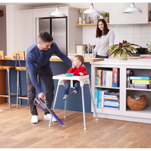 BLACKDECKER BHHV520BFP handheld vacuum cleaning food crumbs near a high chair in a modern kitchen.