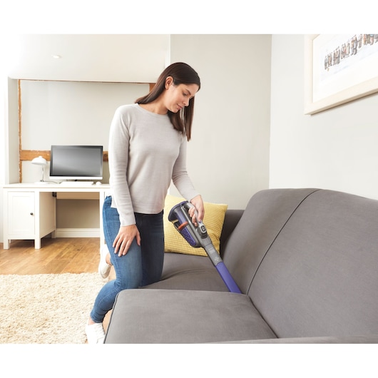 BLACKDECKER BHHV520BFP handheld vacuum in use cleaning a grey sofa in a modern living room.