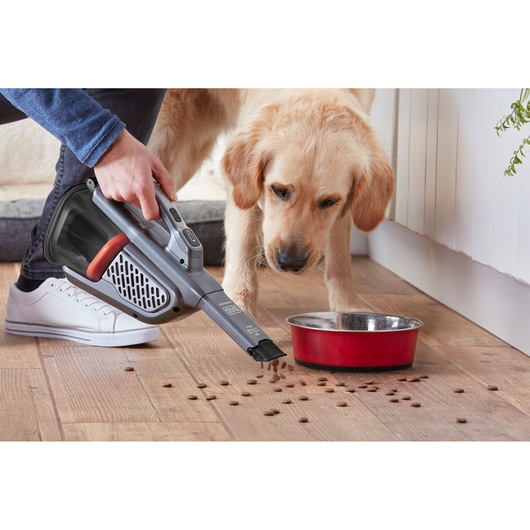 BLACKDECKER BHHV520JF handheld vacuum cleaning pet food near red bowl on wooden floor, indoor scene.
