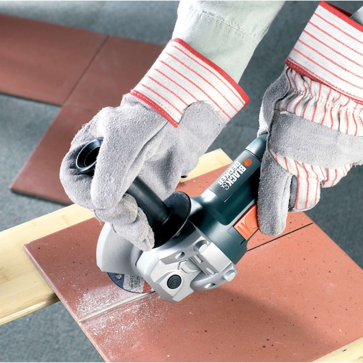 BLACKDECKER CD115 angle grinder cutting brown tile, shown in use with gloves.