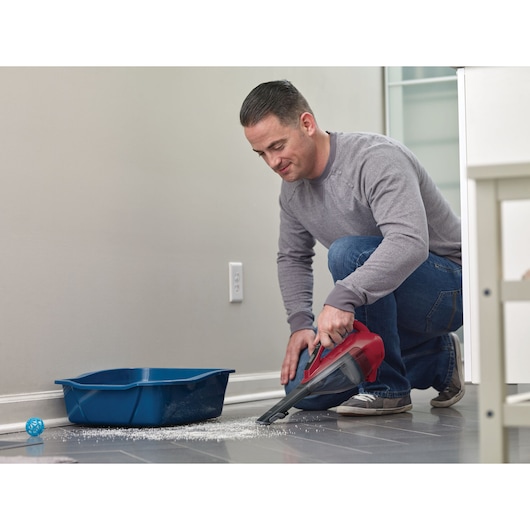 BLACKDECKER DVA315J handheld vacuum cleaning pet litter next to blue tray on tiled floor.
