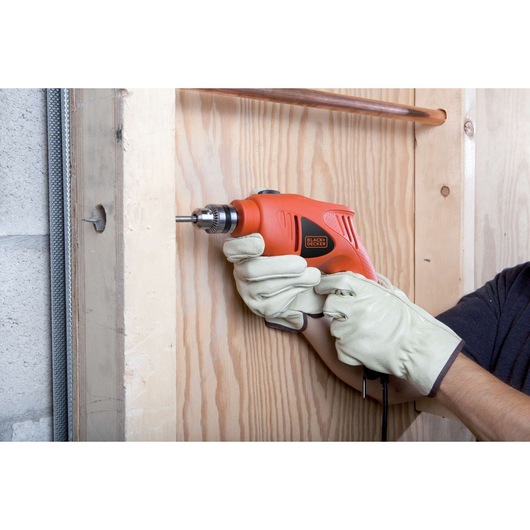 Photo of BLACKDECKER HD5010 orange corded drill used on wooden panel, person wearing work gloves.