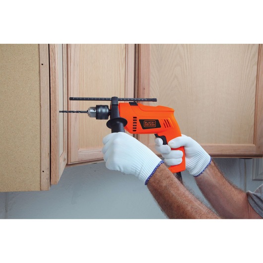 Photo of BLACKDECKER HD555 orange corded drill in use, drilling wood cabinet, gloved hands holding handle.