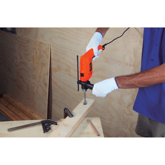 Photo of BLACKDECKER HD555 drill being used on wood, handheld with white gloves in workshop setting.