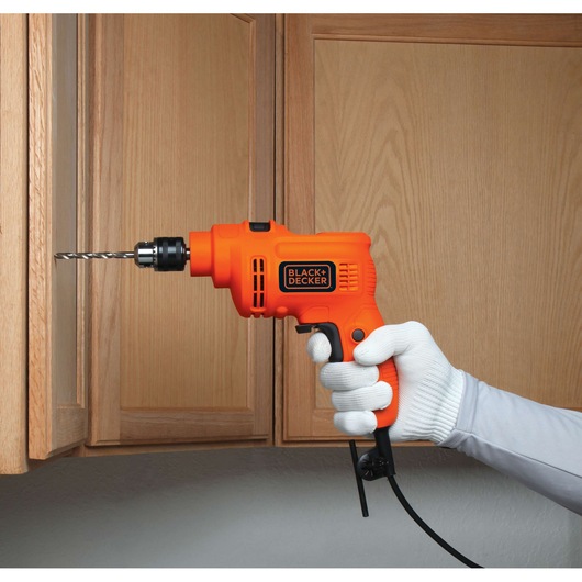 BLACKDECKER KR5010V orange corded drill held by gloved hand drilling into wooden cabinet.