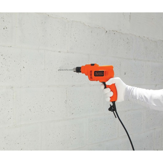 BLACK+DECKER KR5010 orange corded drill in use on a white concrete wall, right side view.