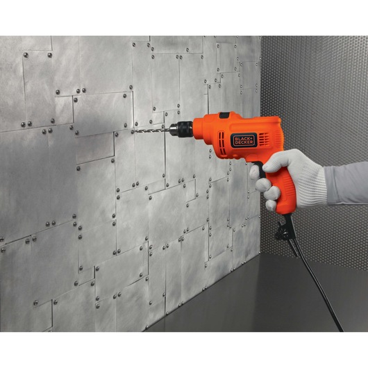 BLACKDECKER KR5010 orange corded drill held against a metal wall, side angle, drilling in progress.