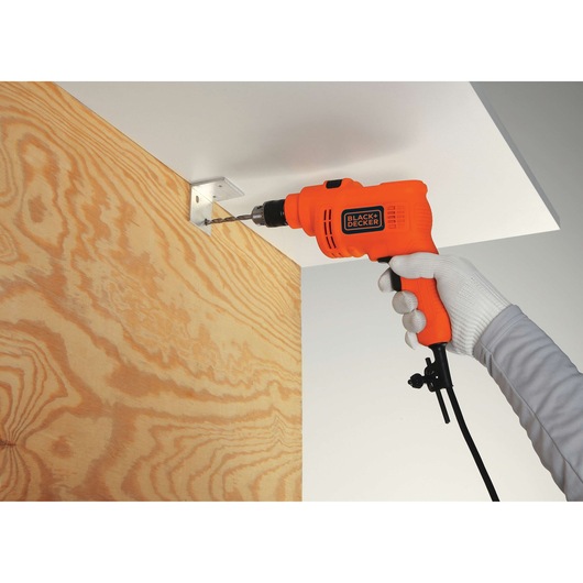 BLACK+DECKER KR5010 electric drill used to drill into a metal bracket on wood, close-up view.