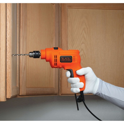 BLACKDECKER KR5010 orange corded drill held by gloved hand drilling into wooden cabinet.