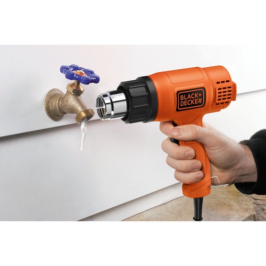 Photo of BLACK+DECKER heat gun KX1650 thawing a frozen outdoor faucet, side angle.