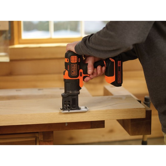 BLACK+DECKER MTJS1 cordless jigsaw in use cutting wood, photography, indoors workshop.