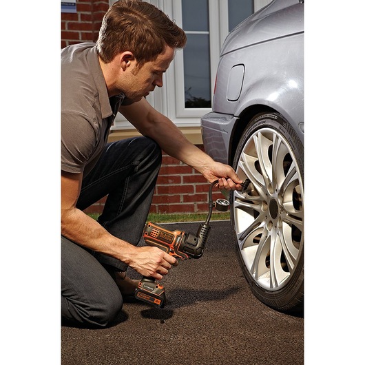 Photo of a person using a BLACKDECKER MTNF9 cordless inflator on a car tire outdoors.