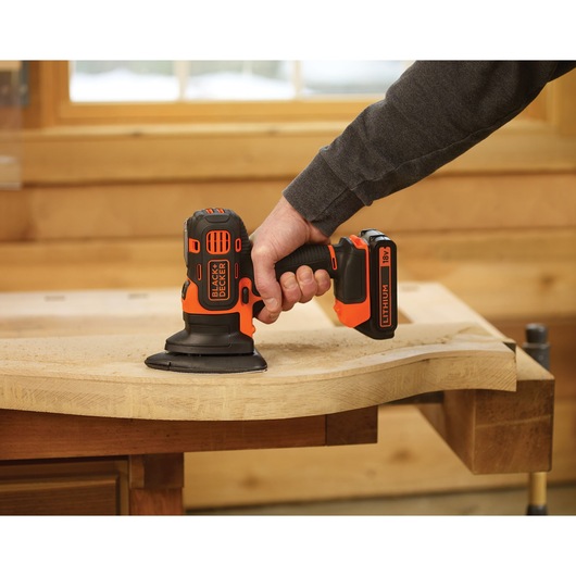 BLACKDECKER MTSA2 cordless sander in use on a wooden surface, orange and black design, workshop setting.