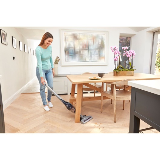 BLACKDECKER SVB520JW cordless stick vacuum in use cleaning crumbs on wooden floor near dining table.