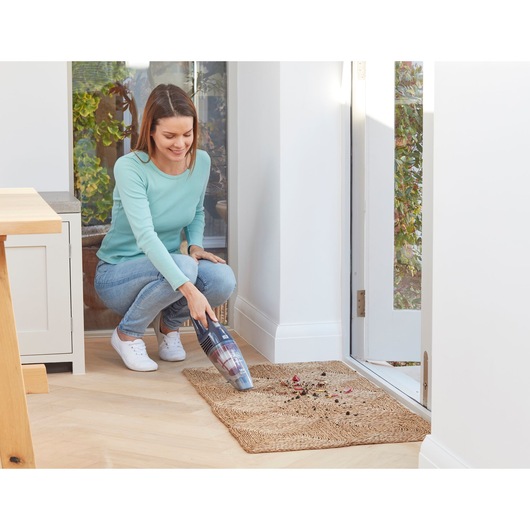 Photo of BLACKDECKER SVB520JW handheld vacuum cleaning dirt from a mat near a doorway.